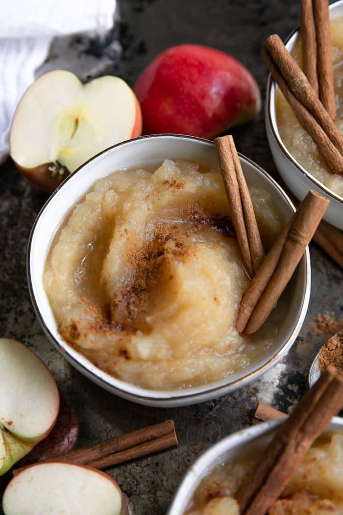 Close-up image of a bowl filled with homemade applesauce made with pink lady apples and topped with ground cinnamon and whole cinnamon sticks.