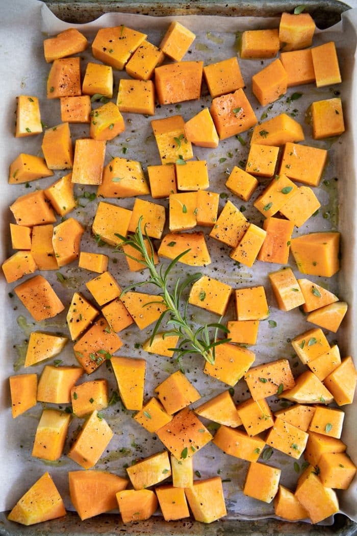 cubes of butternut squash on a baking sheet tossed in oil and herbs