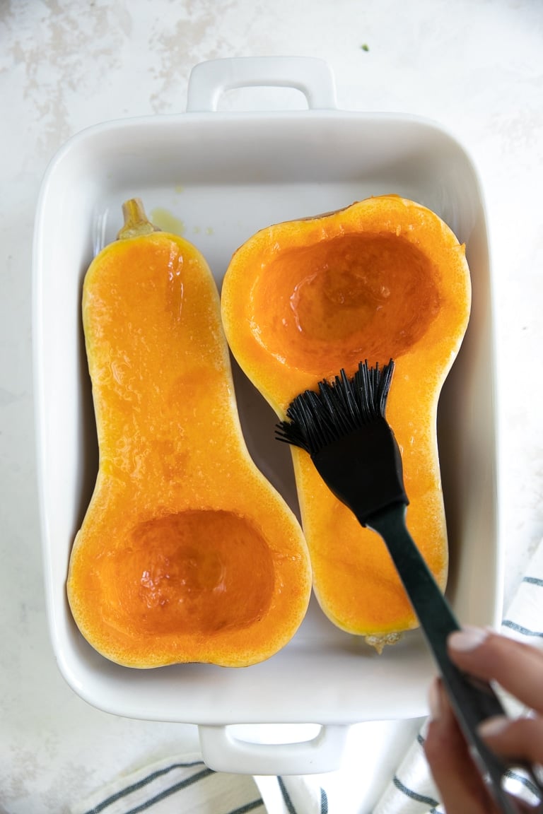 Brushing a halved butternut squash with olive oil