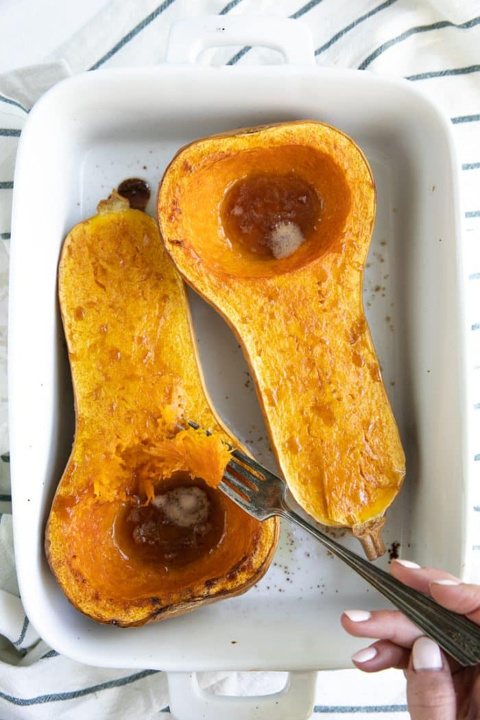 A close up halved roasted butternut squash that has been roasted in a white dish