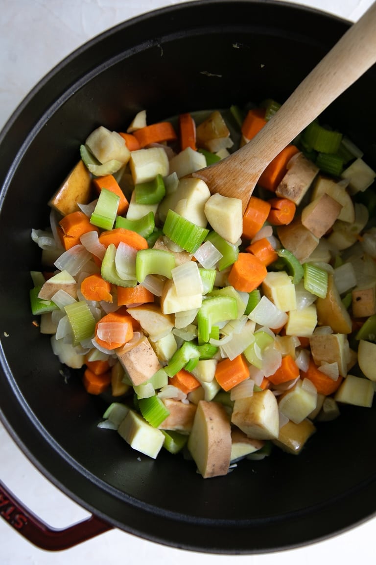 LargeOnion, sweet potato, celery, and carrots cooking in a large heavy-bottomed stock pot.