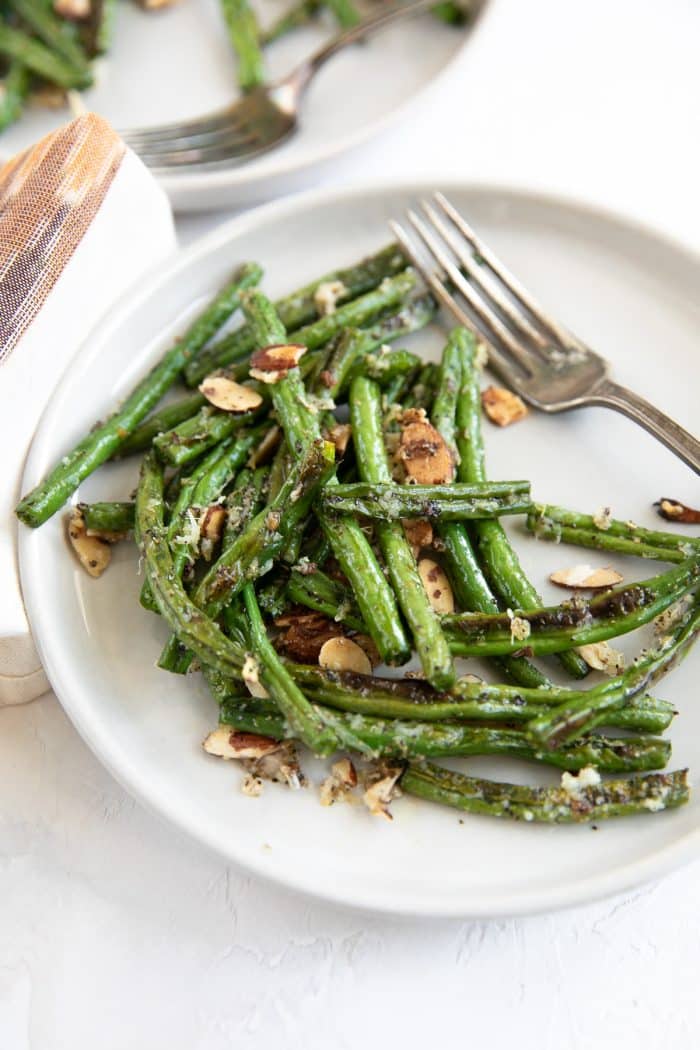 Small serving plate with oven roasted green beans tossed in shredded parmesan cheese and candied slivered almonds.