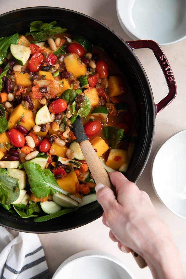 Hand holding a large rubber spatula stirring a big pot of butternut squash chili