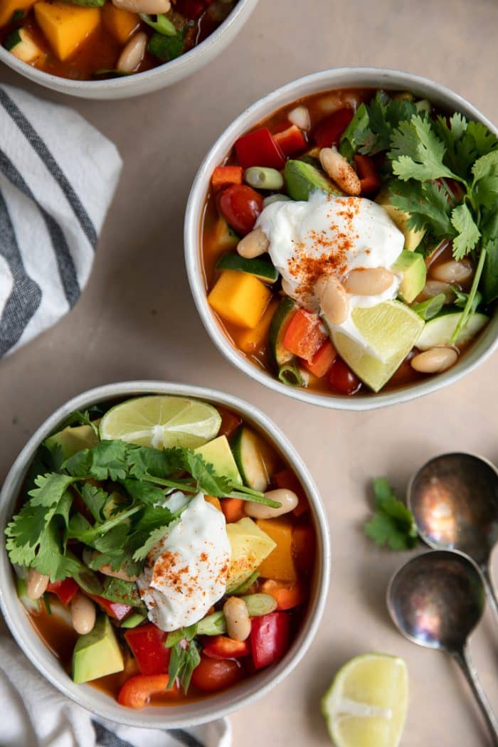 White bowls filled with butternut squash packed with beans, bell pepper, green onion, cilantro, soup cream, and avocado.