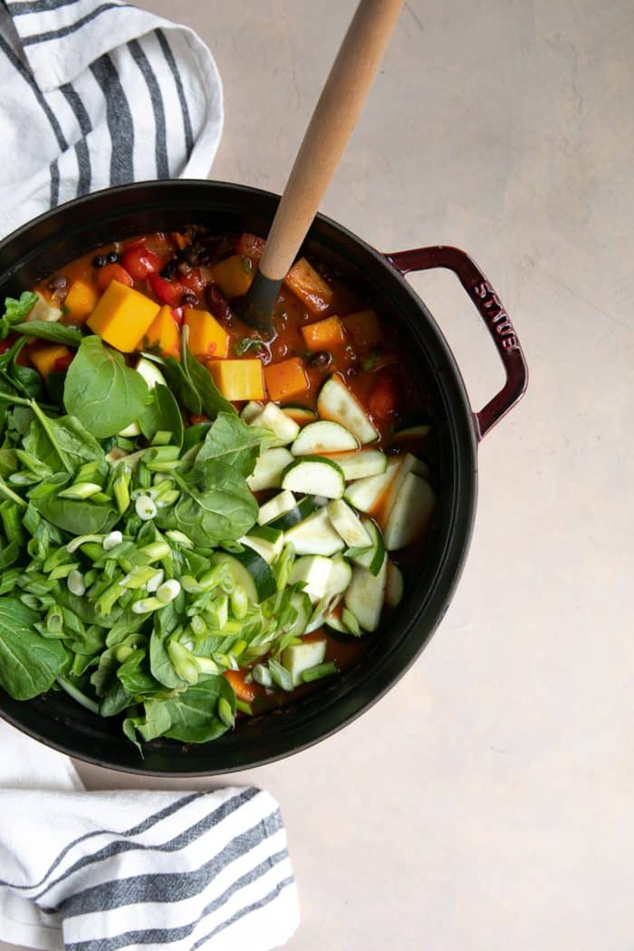 Large Staub Dutch oven filled with butternut squash chili and fresh spinach