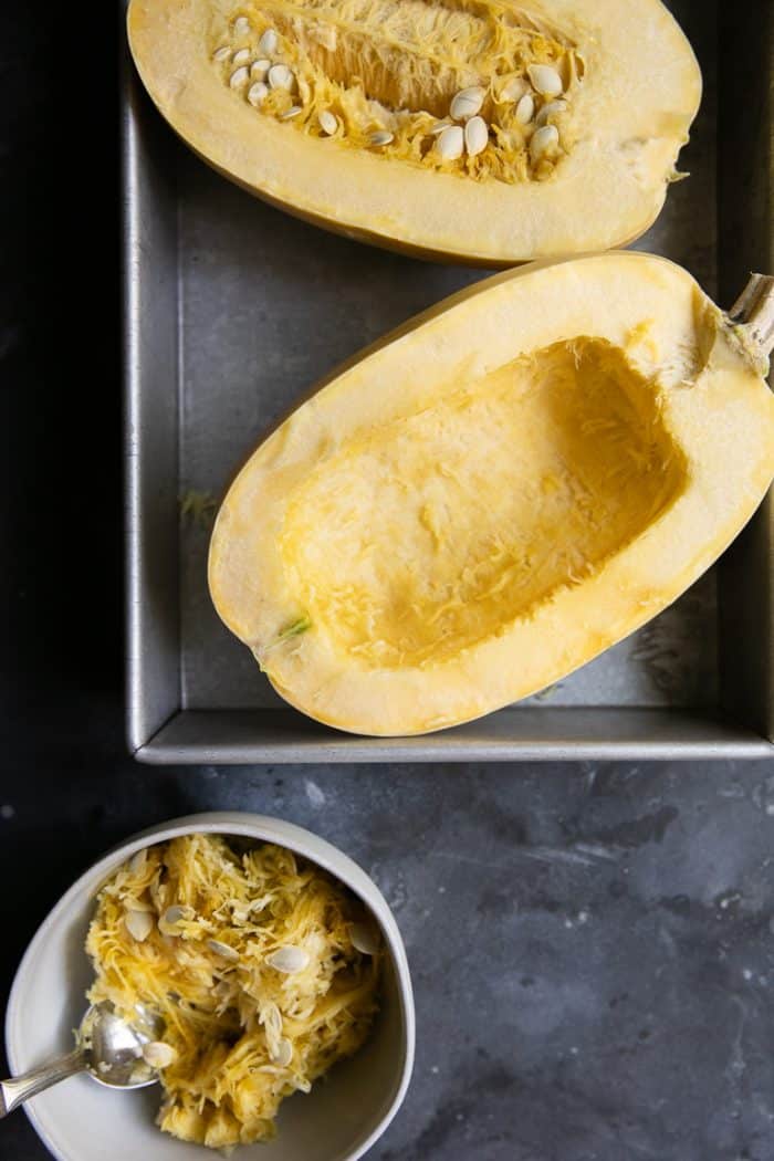 Halved spaghetti squash. One half with seeds scooped out into a bowl and the other with the seeds intact.