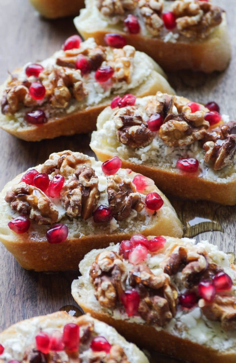Serve board filled with Crostini topped with goat cheese, toasted walnuts, pomegranate arils, and honey.