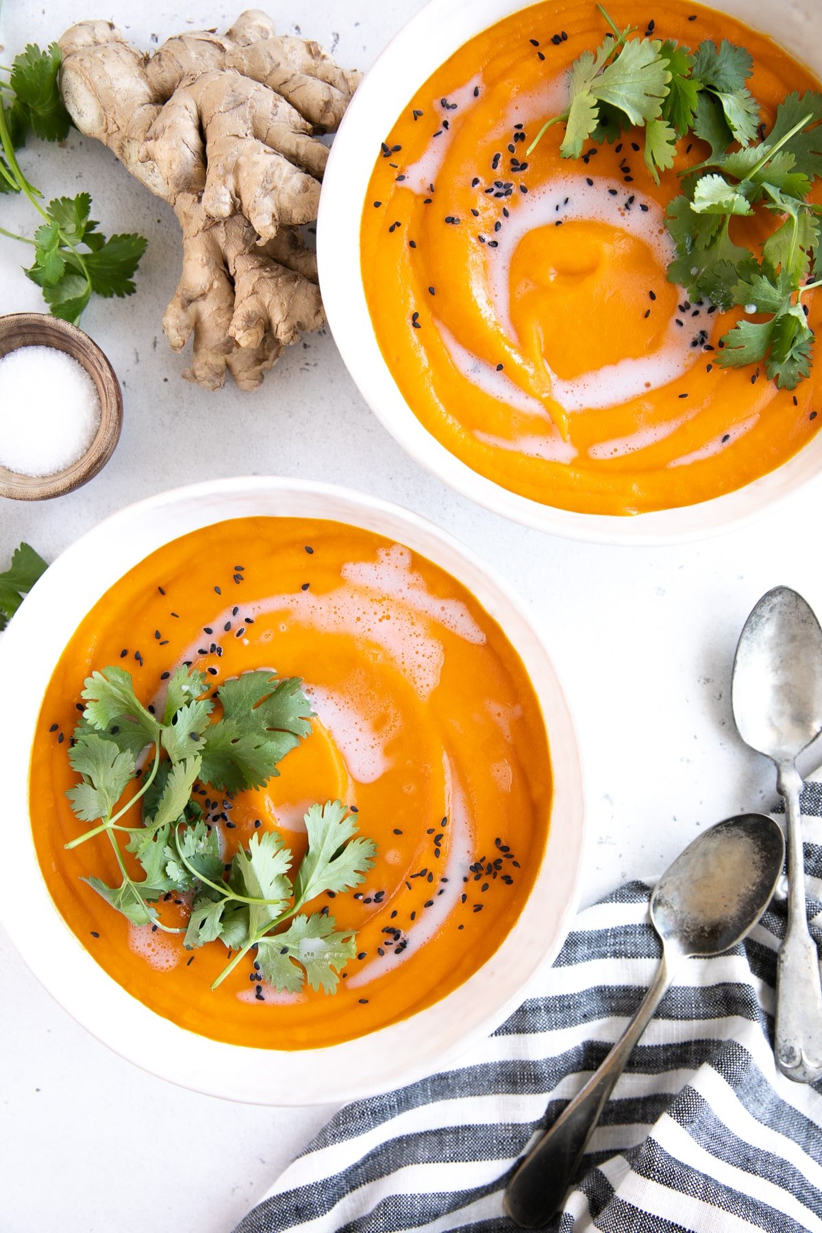 Two white soup bowls filled with ginger carrot soup and garnished with coconut cream, cilantro, and black sesame seeds.