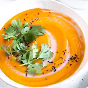 Two white soup bowls filled with ginger carrot soup and garnished with coconut cream, cilantro, and black sesame seeds.