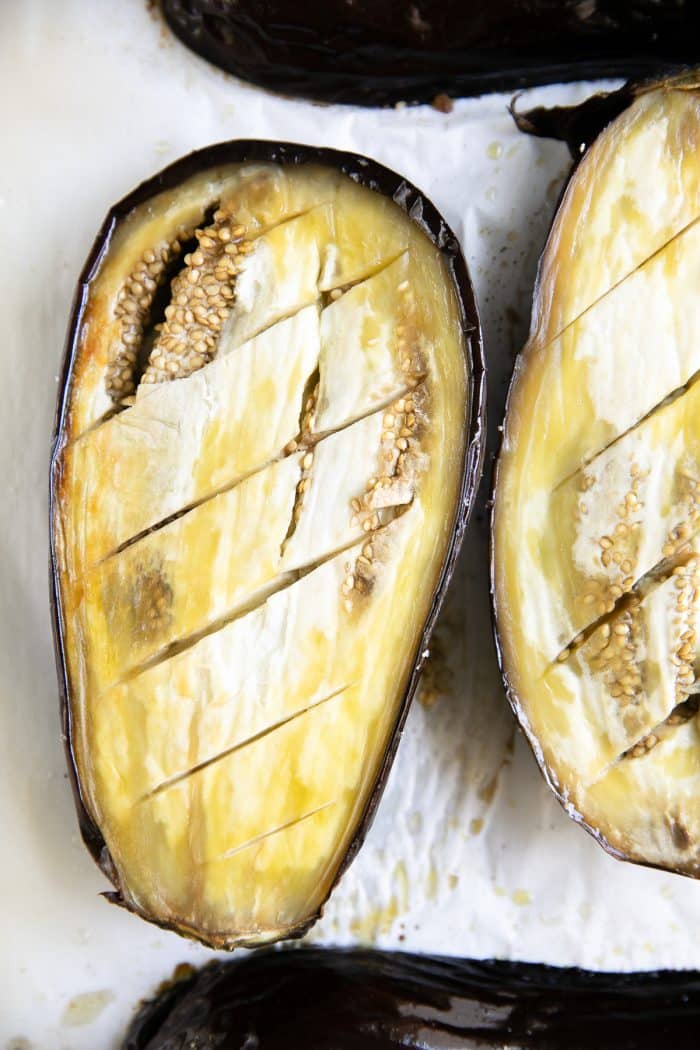 Roasted eggplant halves skin-side-up on a large baking sheet