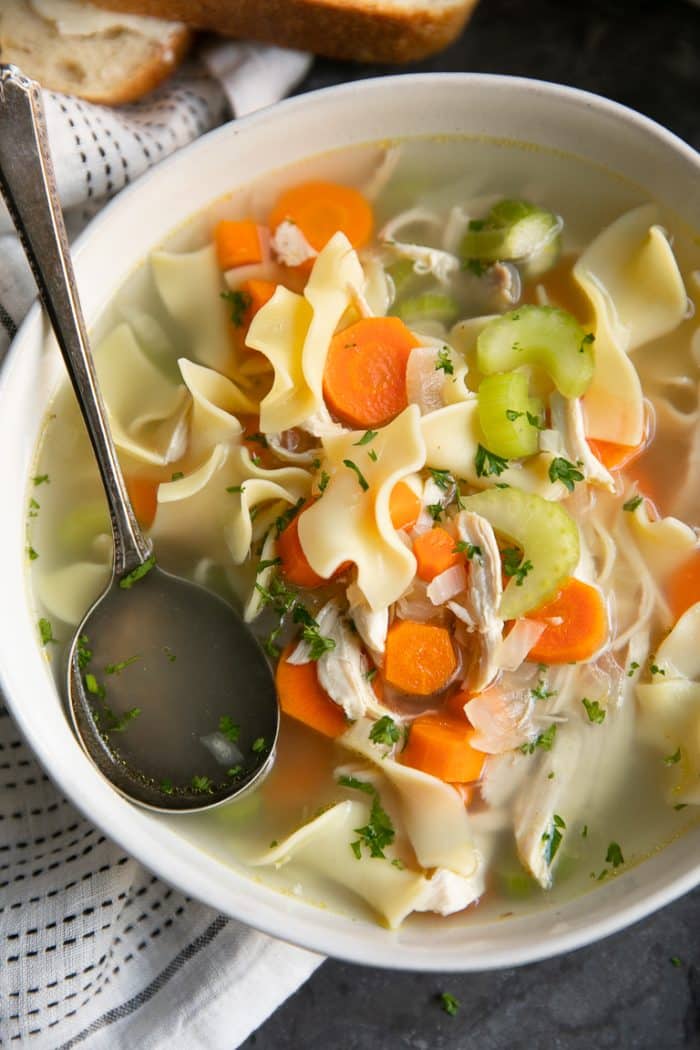 Bowl of chicken noodle soup garnished with chopped parsley.
