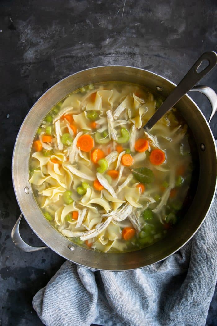 Large pot filled with homestyle chicken noodle soup made with homemade chicken stock, carrots, celery, onion, chicken, and egg noodles.