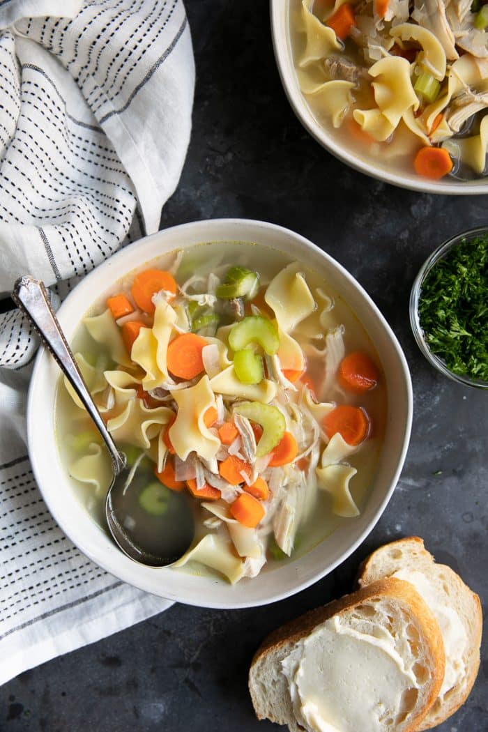 Overhead image of a white owl filled with homemade chicken noodle soup with carrots, celery, and onions.