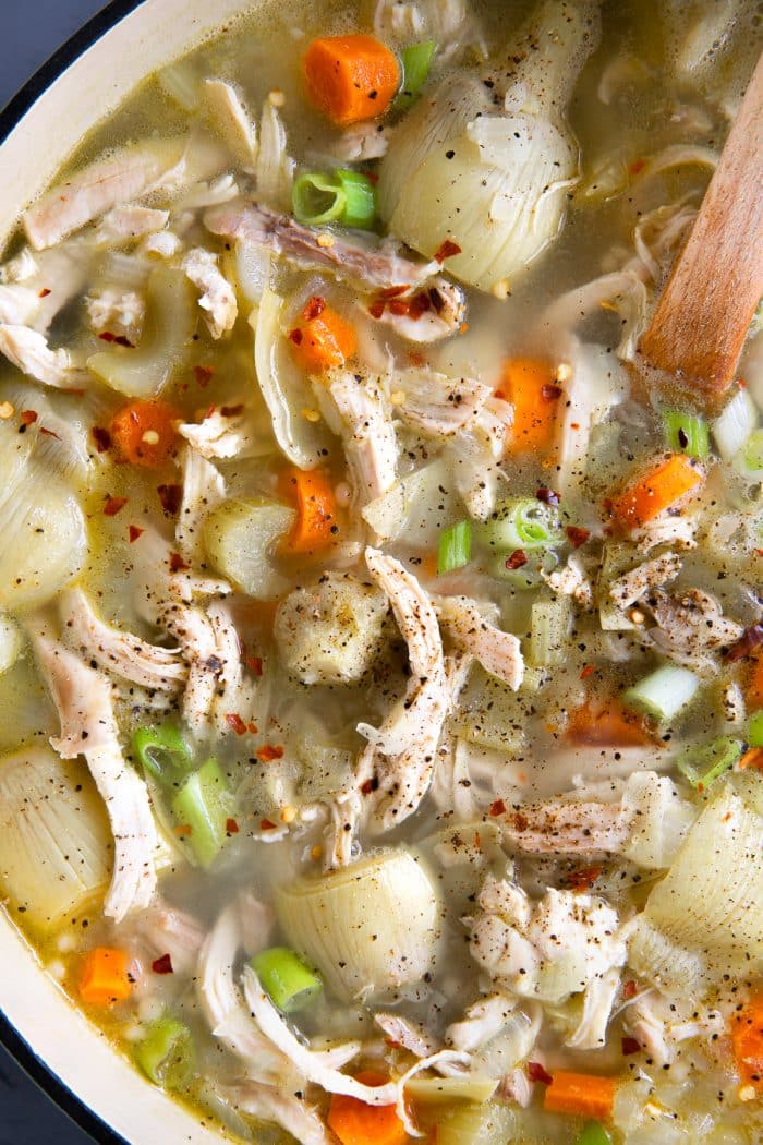 Close-up image of a large pot of chicken soup made with lemon juice, chicken broth, shredded chicken, carrots, celery, and artichoke hearts.