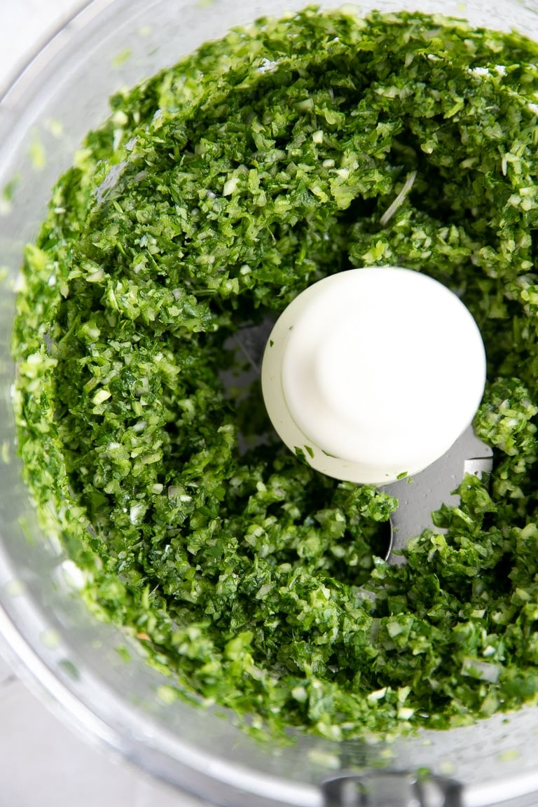 Food processor filled with finely processed coriander, garlic, and shallots.