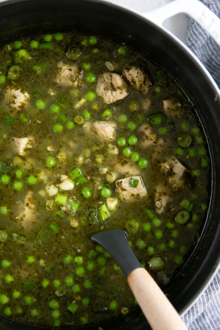 Large white pot filled with Peruvian Chicken Soup filled with peas and corn.