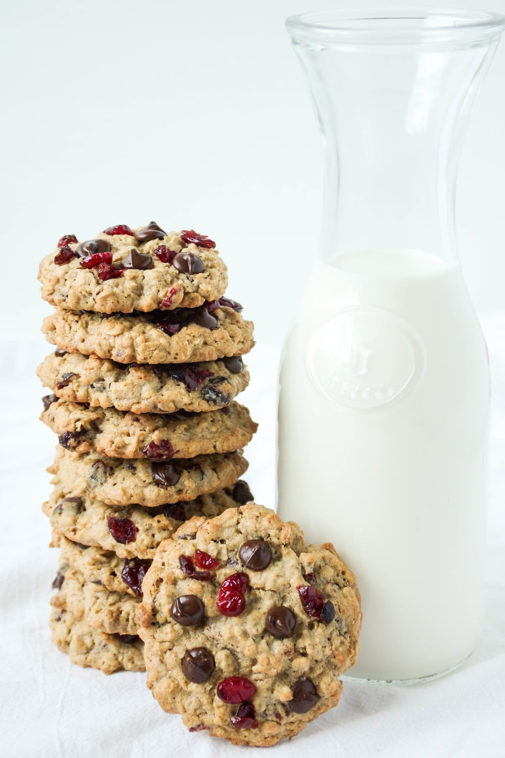 Large stack of cranberry chocolate chip cookies with a big jug of milk.