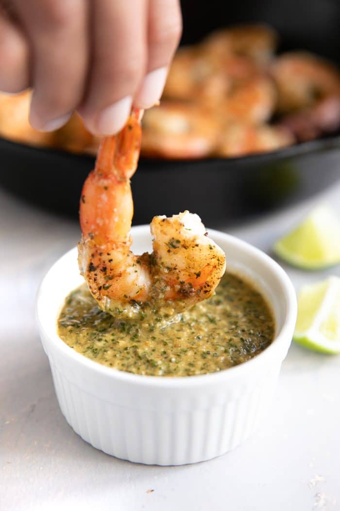 Large cooked shrimp being dipped into cilantro lime sauce.