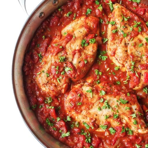 Large skillet filled with homemade roasted red pepper sauce and three whole chicken breasts garnished with chopped parsley.