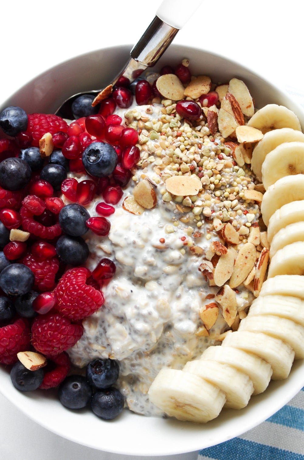 Overhead photo of white bowl with vanilla overnight oats loaded with berries, pomegranate arils, and sliced banana.