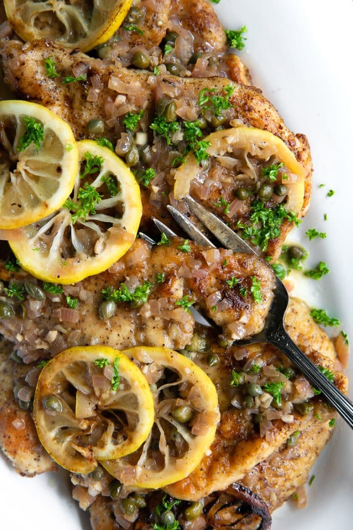 Serving dish with chicken piccata cutlets topped with piccata sauce and fresh lemon slices.