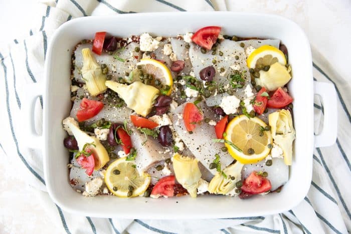 The Mediterranean fish in a white casserole dish with lemons, capers in another layer