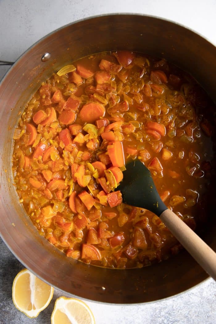 Adding the tomatoes, lemon juice, and lemon zest to the Moroccan chicken stew pot
