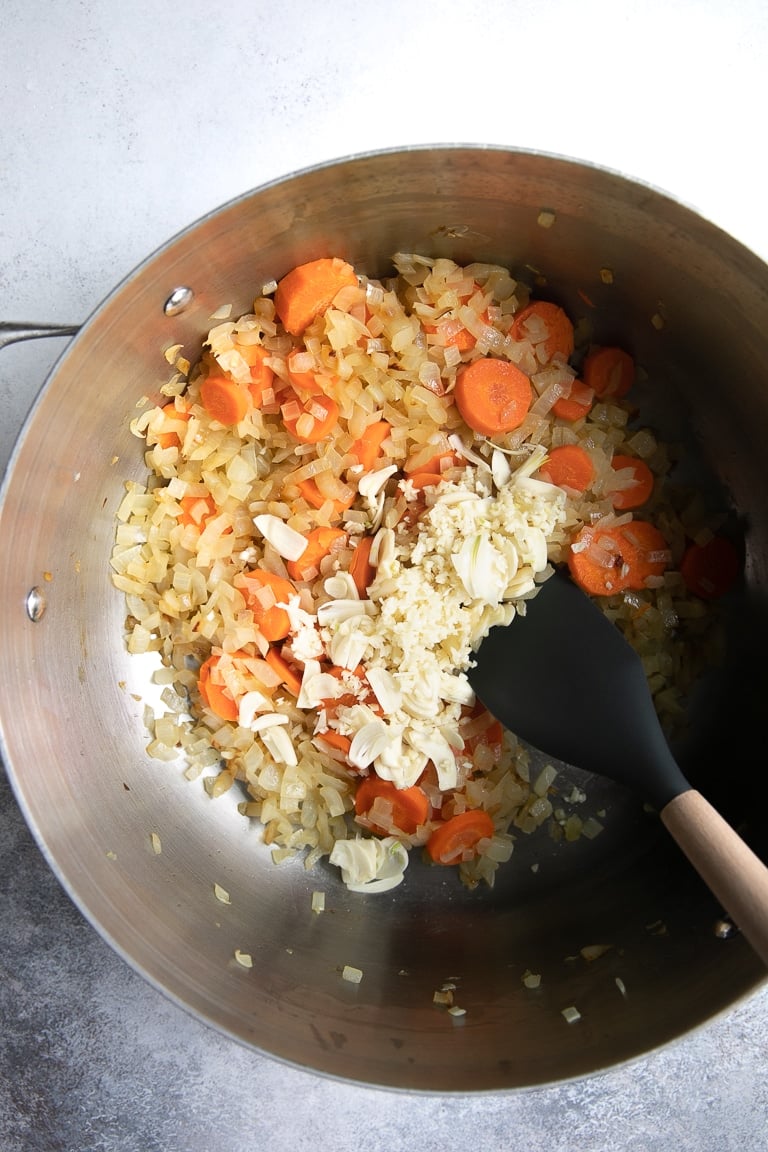 a pot with onions carrots being cooked and stirred