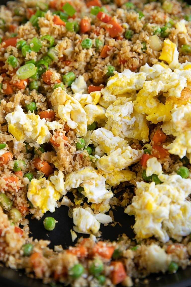 Scrambled eggs being added to cooked cauliflower fried rice.