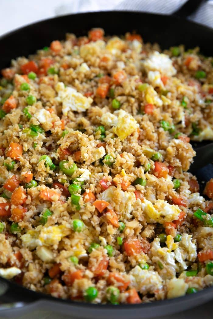 Cauliflower fried rice cooking in a black skillet.