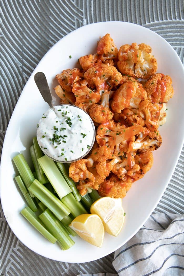 Large platter with baked buffalo cauliflower, celery sticks, ranch dressing, and lemon wedges.