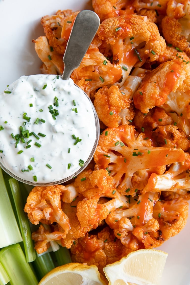 White plate with baked buffalo cauliflower and ranch dressing.