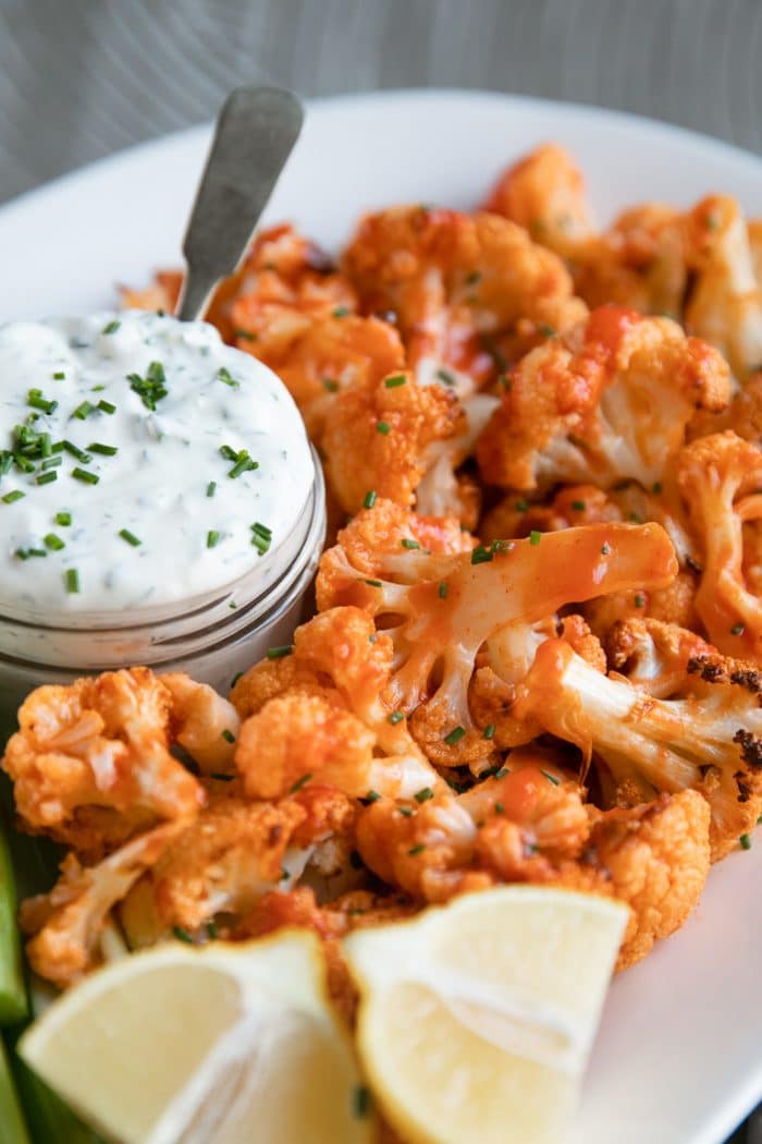 Baked buffalo cauliflower with ranch dressing and lemon wedges.