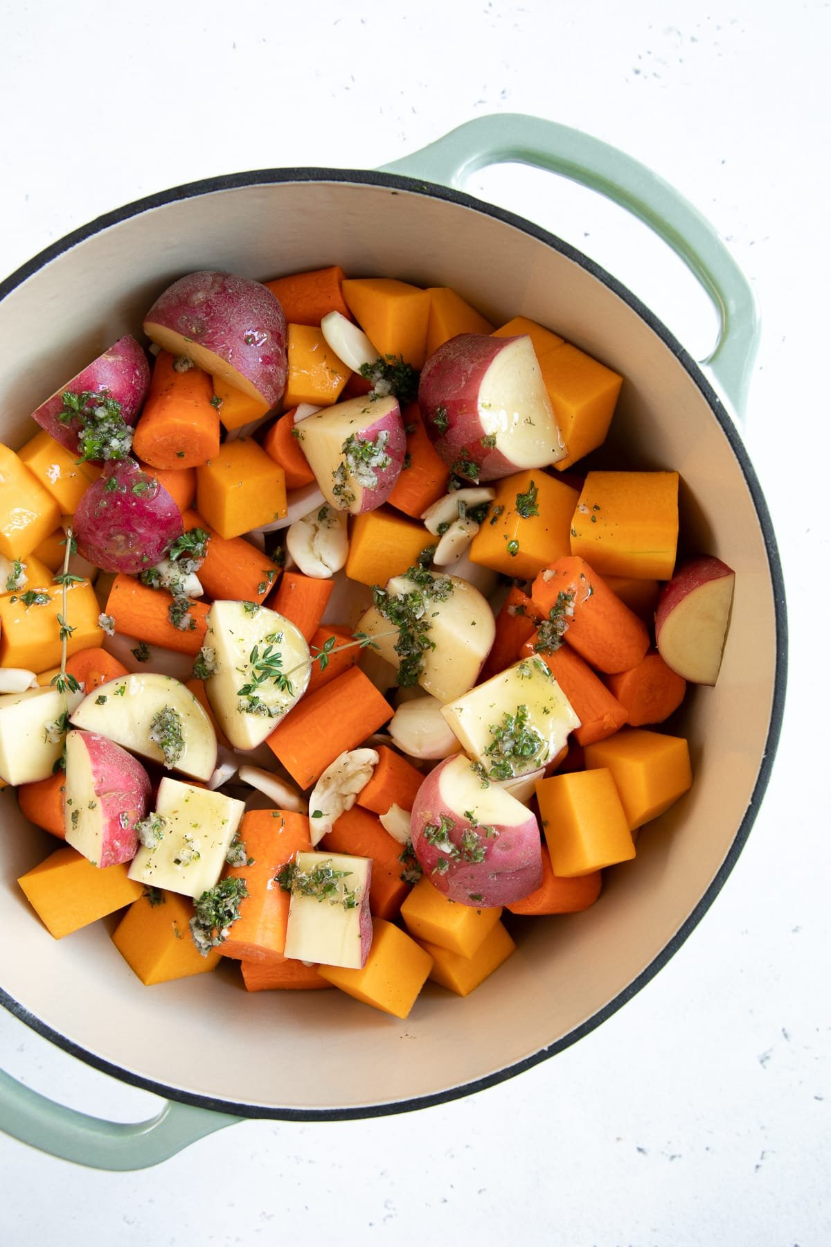 Large Dutch oven filled with chopped potatoes, carrots, and butternut squash and drizzled with garlic herb and butter sauce.