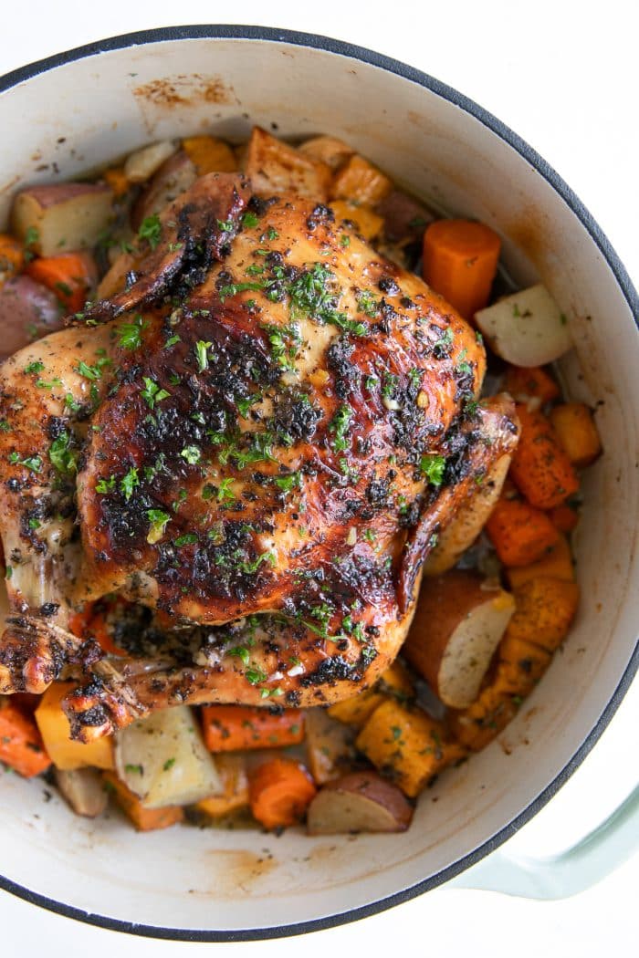 Roast chicken in a large round Dutch oven set atop a bed of vegetables.