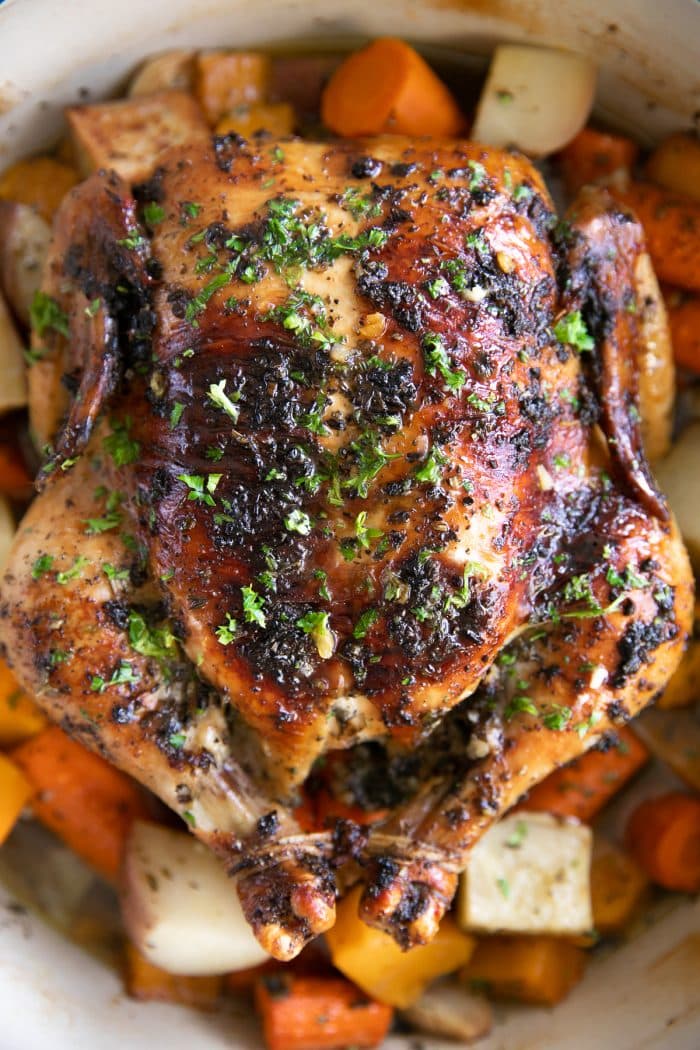 Garlic Herb Butter Roast chicken in a large round Dutch oven set atop a bed of vegetables.