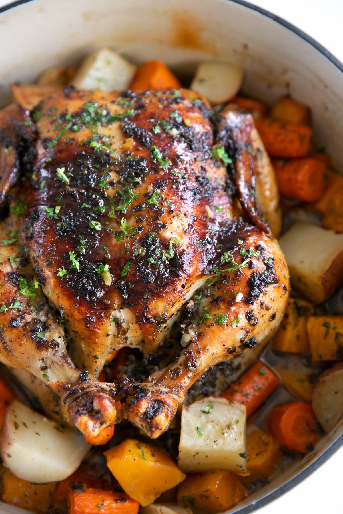 Perfect Roast chicken in a large round Dutch oven set atop a bed of vegetables.