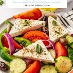 Pinterest pin image of classic Greek salad with tomato wedges, cucumber rounds, red onion, green bell pepper, Kalamata olives, and large triangular slabs of feta cheese topped with dried oregano and fresh oregano leaves. A white text overlay reads โCLASSIC GREEK SALADโ and โTHEFORKEDSPOON.COM.โ