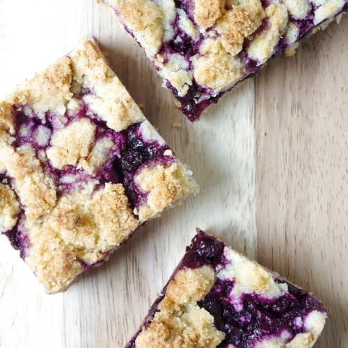 A piece of blueberry crumble bar sitting on top of a wooden cutting board