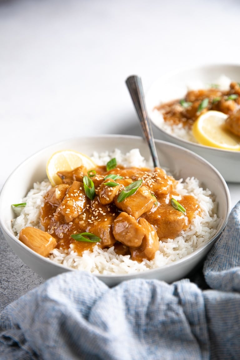 Shallow white bowl filled with white rice and topped with Lemon Honey Ginger Chicken garnished with green onions and sesame seeds.