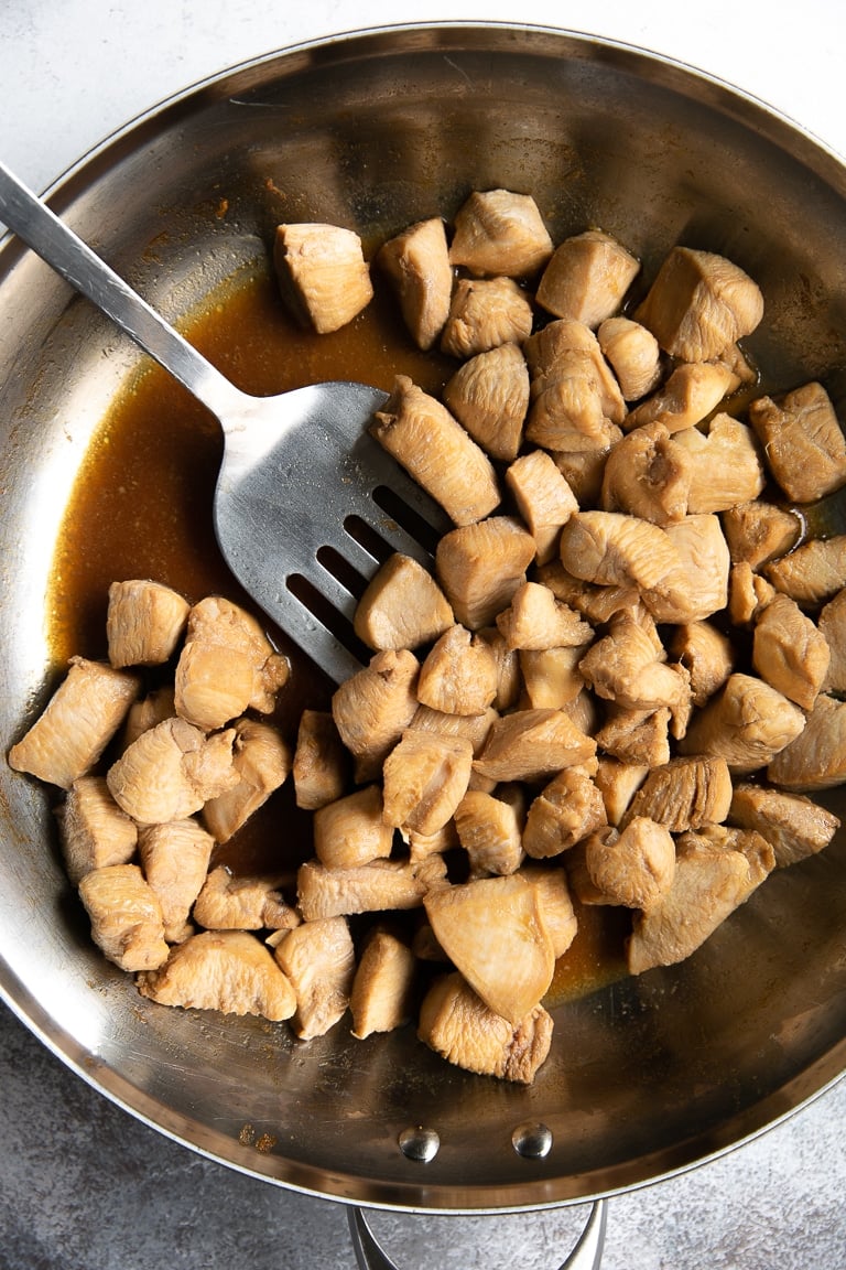 Skillet filled with cubes of cooked marinated chicken.
