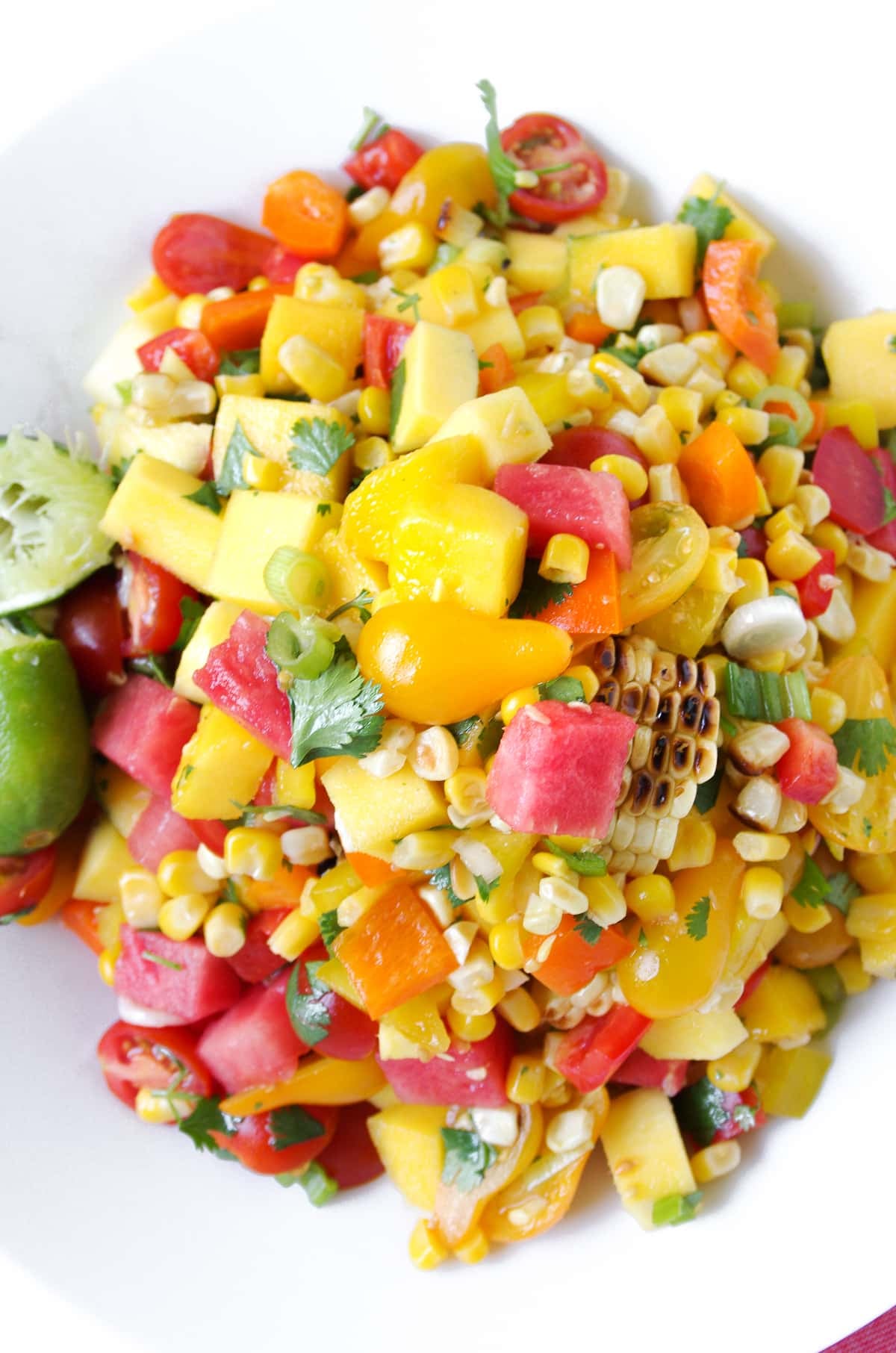 Large white bowl filled with a chopped salad made with grilled corn, watermelon and mango cubes, cherry tomatoes, cilantro, and fresh lime juice.
