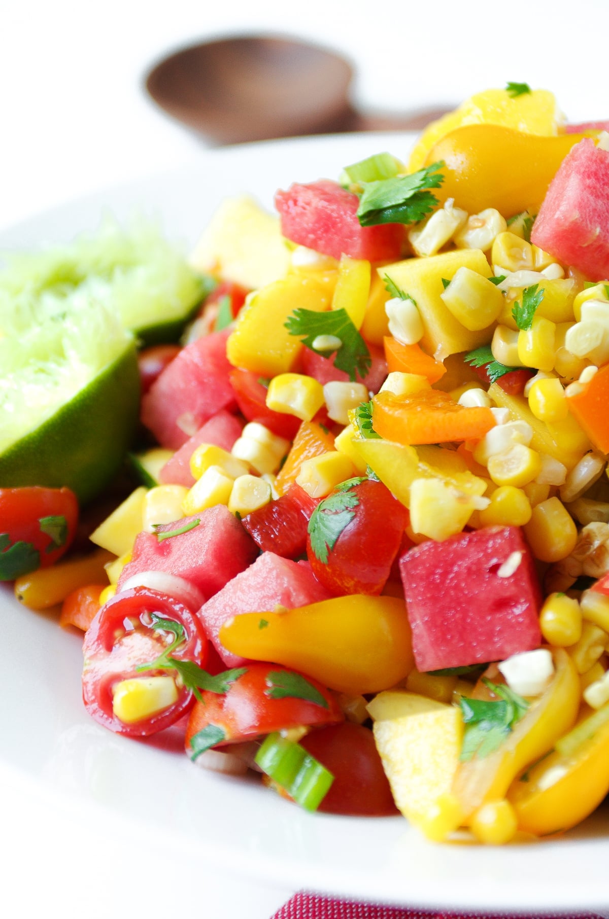 Large white bowl filled with a chopped salad made with grilled corn, watermelon and mango cubes, cherry tomatoes, cilantro, and fresh lime juice.