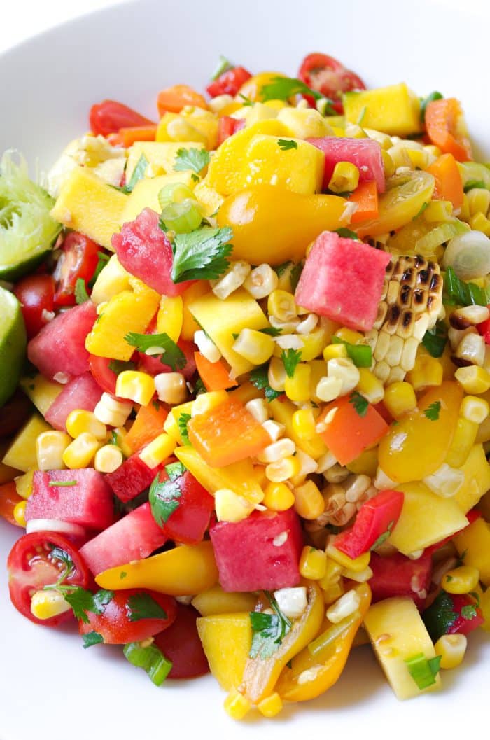 Large white bowl filled with a chopped salad made with grilled corn, watermelon, mango, cherry tomatoes, cilantro, and fresh lime juice.