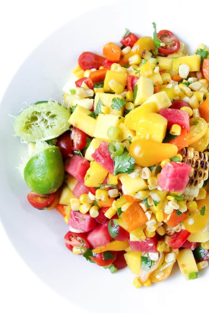 Large white bowl filled with a chopped salad made with grilled corn, watermelon, mango, cherry tomatoes, cilantro, and fresh lime juice.