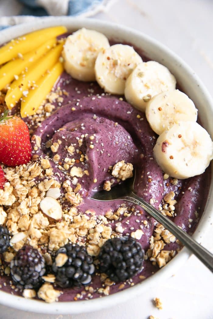 Spoon in acai bowl decorated with fresh fruit and granola.