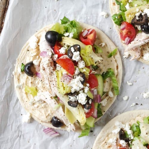 Easy Mediterranean Chicken Wraps made with hummus, salad, feta cheese, and chicken on parchment paper