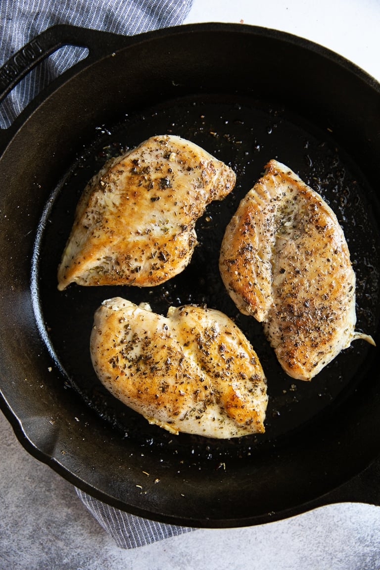 Image of three fully cooked chicken breasts in a large cast iron skillet.