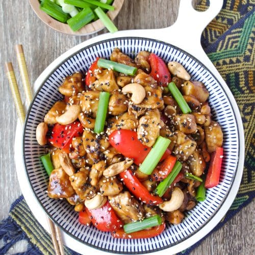Cashew Chicken in a large blue and white serving bowl garnished with sesame seeds and green onions.