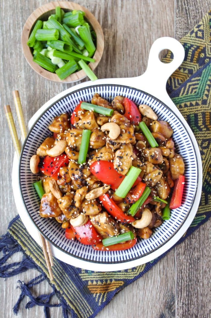 Cashew Chicken in a large blue and white serving bowl garnished with sesame seeds and green onions.